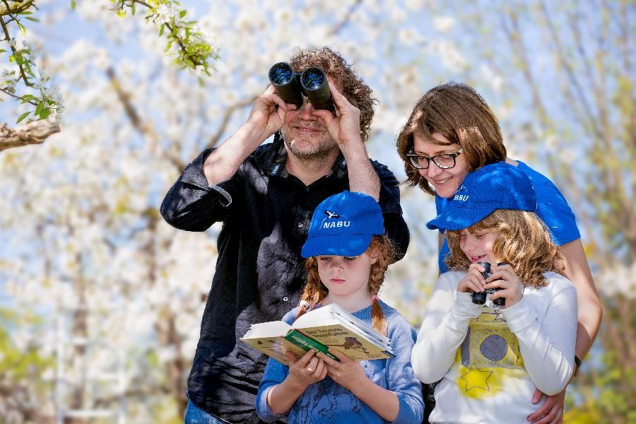 Hier ist eine Familie mit zwei Kindern zu sehen, die im Frühlingsgarten auf Vogelbeobachtung gehen.