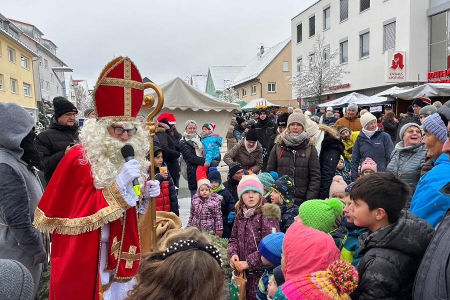 Der Nikolaus in rotem Gewand umringt von vielen Kindern und Erwachsenen verteilt Süßigkeiten.       