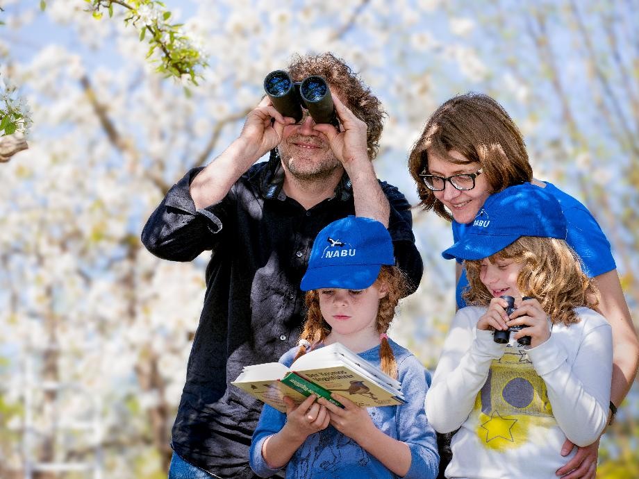 Hier ist eine Familie mit zwei Kindern zu sehen, die im Frühlingsgarten auf Vogelbeobachtung gehen.                  