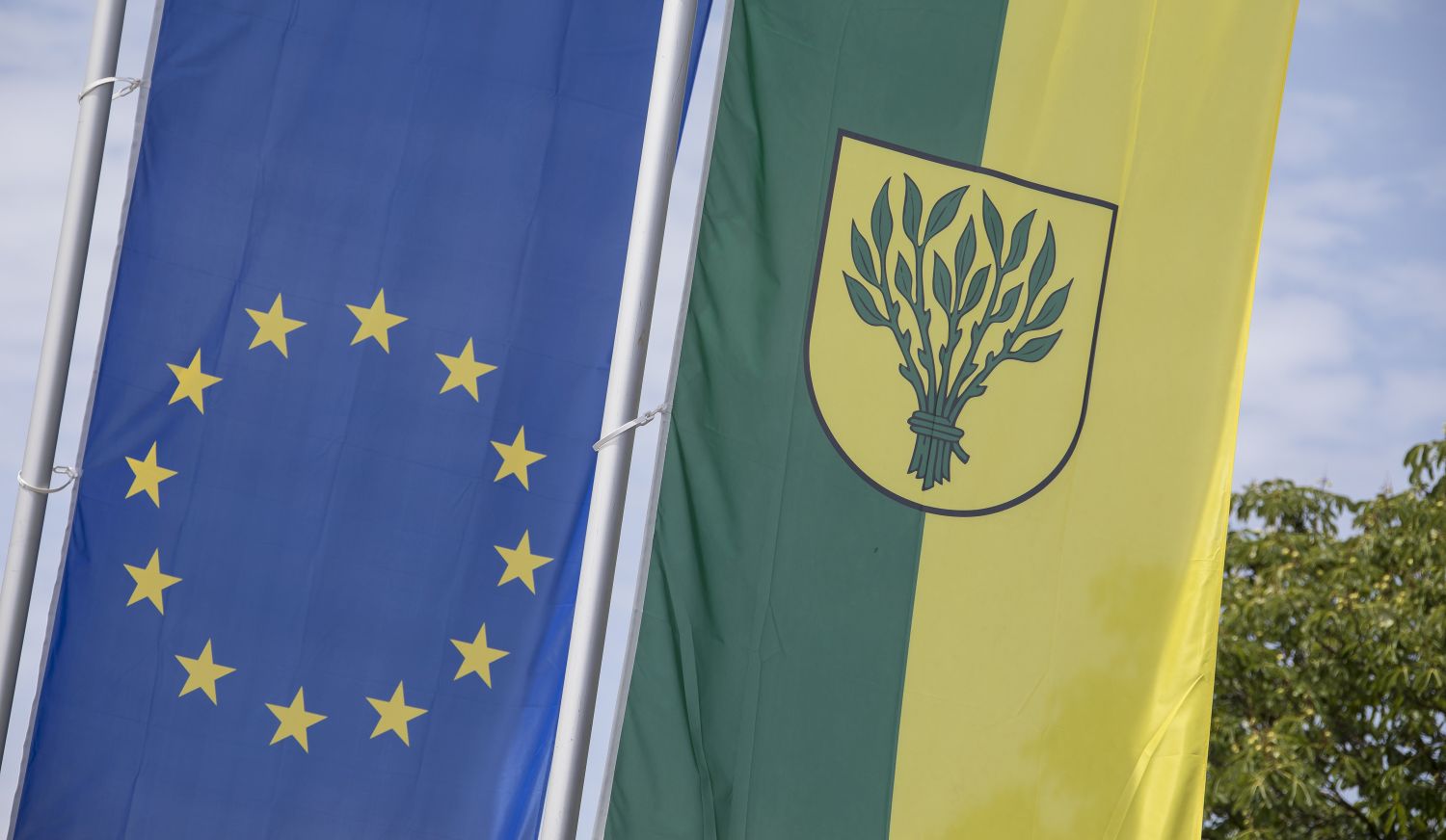 Zu sehen ist links die blaue Europa-Flagge mit im Kreis angeordneten gelben Sternen und rechts die gelb-grüne Flagge mit dem Wappen der Stadt Rutesheim.             