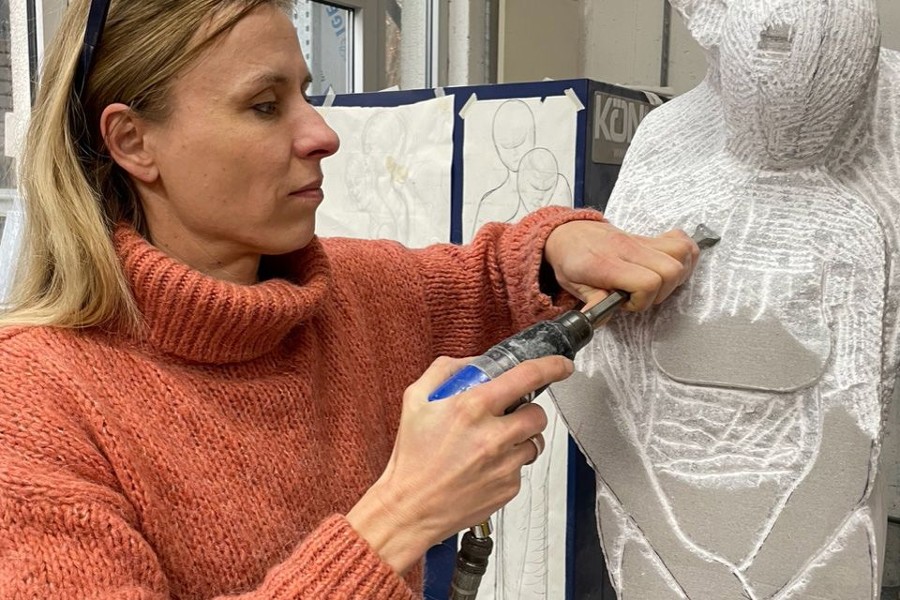 Zu sehen ist die Künstlerin Katja Geisselhardt, die in ihrer Werkstatt eine weiße Steinskulptur bearbeitet.