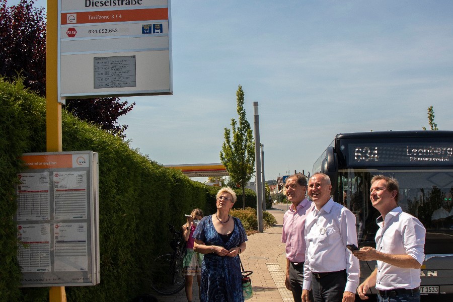 Bürgermeisterin Susanne Widmaier, Erster Beigeordneter Martin Killinger sowie zwei weitere Personen begutachten die neue Fahrgastinformationsanzeige an einer Bushaltestelle.                       