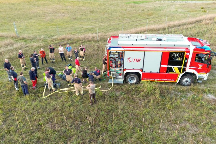 Gruppenbild der Helferinnen und Helfer stehend auf einer Wiese neben einem roten Feuerwehrfahrzeug.