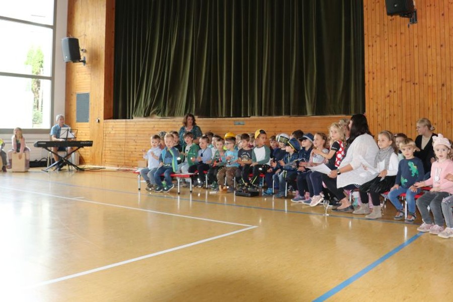 Viele Kindergartenkinder und ihre Erzieherinnen sitzen auf Stühlen und klatschen und singen.