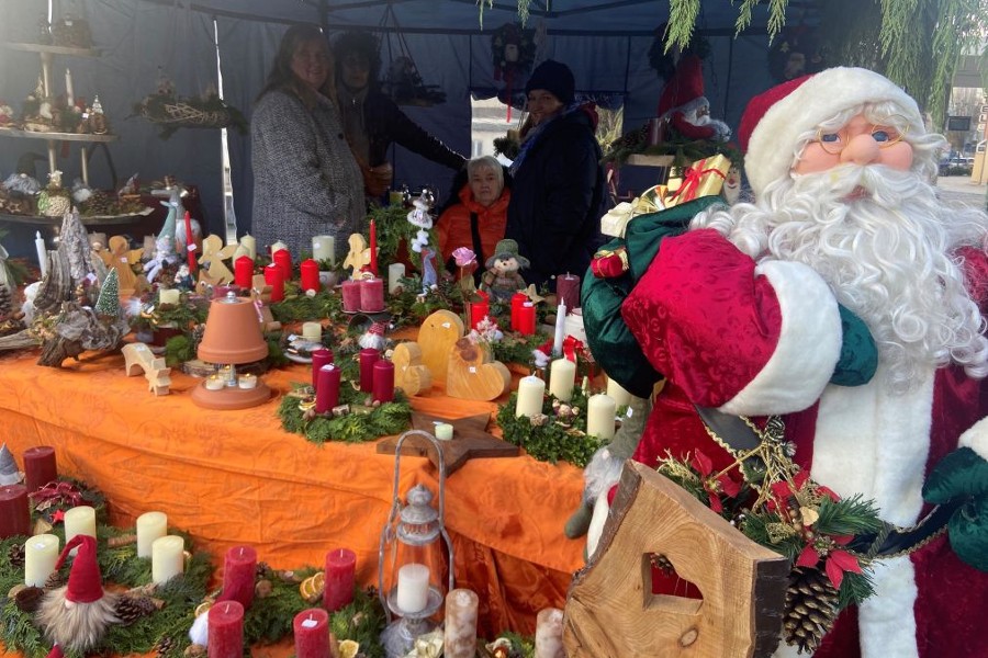 Zu sehen ist ein weihnachtlich geschmückter Verkaufsstand mit einem Nikolaus als Dekoration, Adventskränzen und Deko-Holzartikeln.              