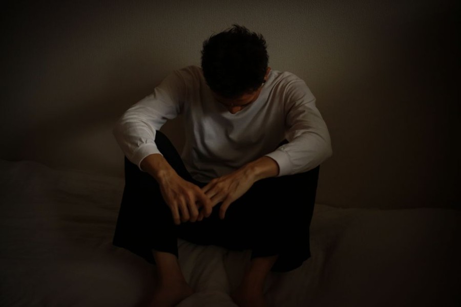 Ein junger Mann sitzt auf dem Boden in sich versunken in düsterer Umgebung vor einer Wand.