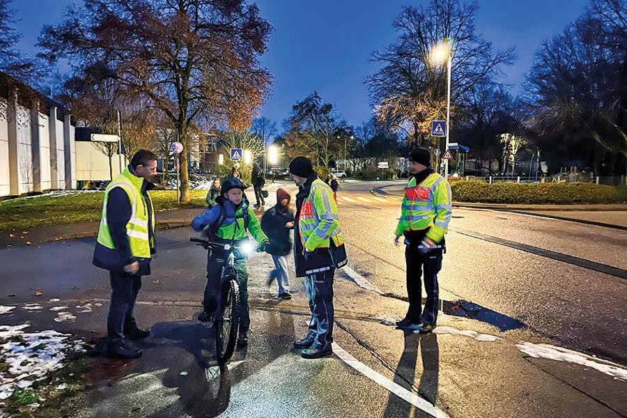 Personen von Polizei und Ordnungsamt in gelben Warnwesten kontrollieren das Fahrrad eines Schülers.            