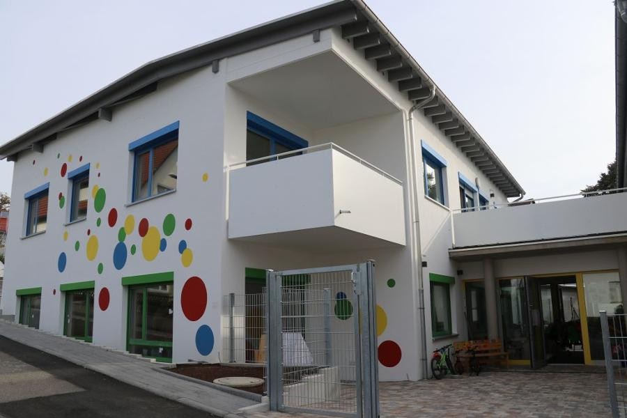 Blick auf das Gebäude des Kindergartens Perouse mit weißer Fassade, auf die bunte Kreise gemalt sind.
