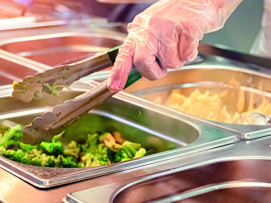 Zu sehen ist eine Hand mit einer Küchenzange, die in ein Warmhaltegefäß aus Metall gefüllt mit Broccoli greift.                 
