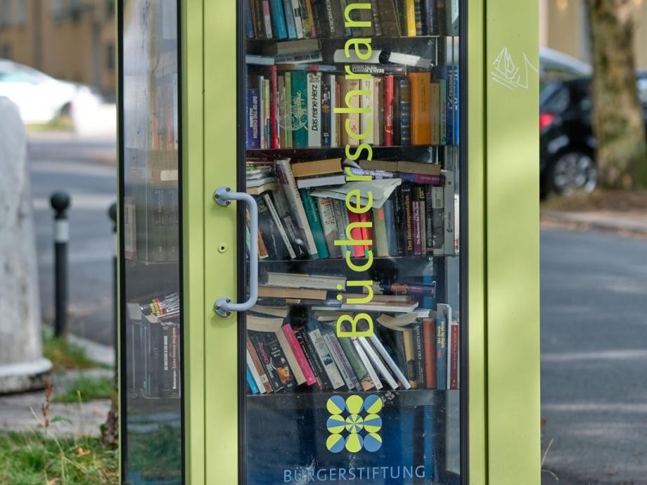 Zu sehen ist ein grüner Bücherschrank aus Metall mit Glasfenstern, der aussieht wie früher die Telefonzellen.