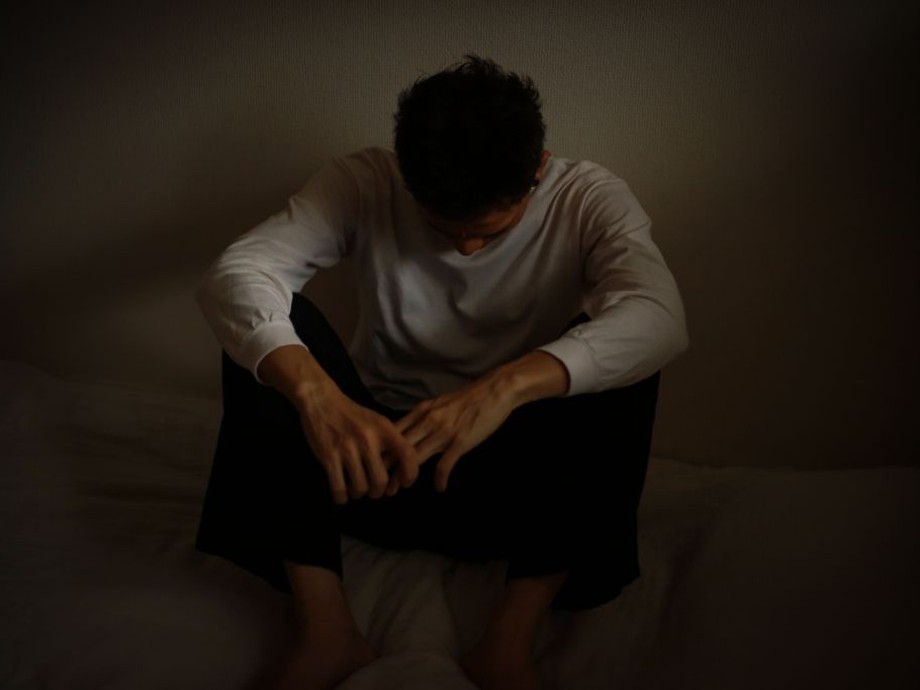 Ein junger Mann sitzt auf dem Boden in sich versunken in düsterer Umgebung vor einer Wand.