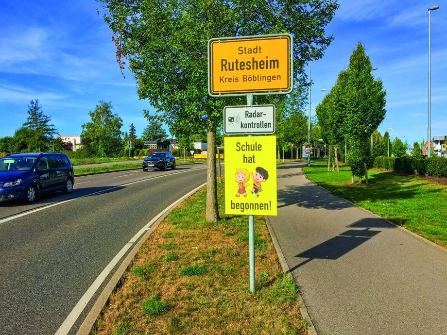 Blick die Ortseingangstafel von Rutesheim mit einem gelben Warnschild Schule hat begonnen.          