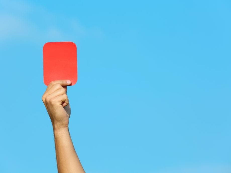 Eine Hand streckt eine rote Karte in den blauen Himmel.