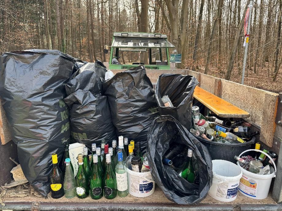 Müll-250321 Hier sind schwarze Müllsäcke und viele leere Flaschen auf einem Traktoranhänger zu sehen.