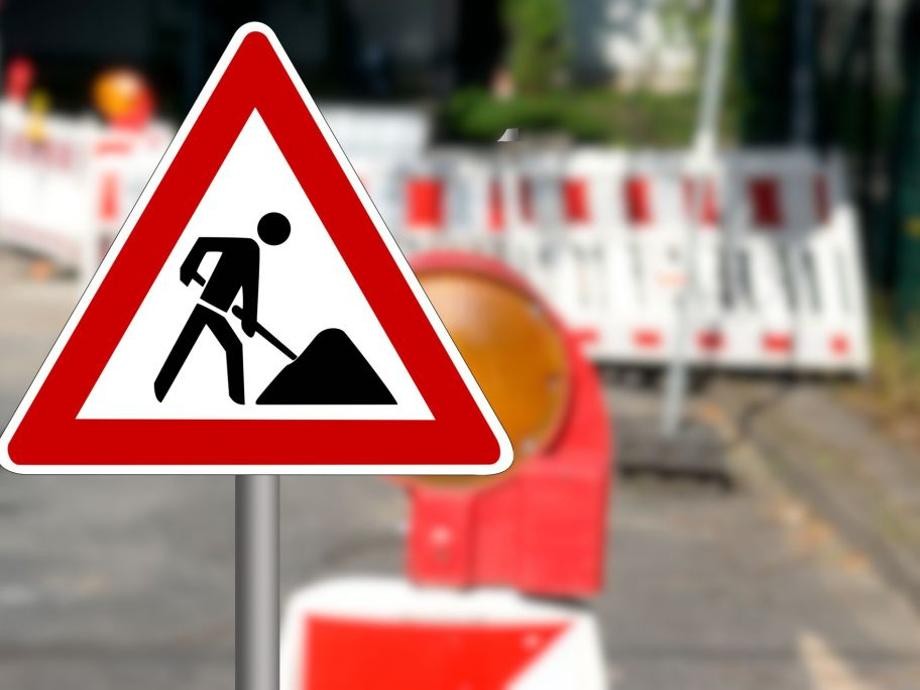 Baustelleninfo Rot-weiße Baustellenabsperrung und im Vordergrund ein dreieckiges Schild rot-weiß umrandet mit schwarzem Männchen, das eine Schaufel hält.