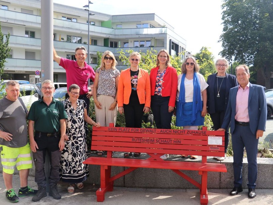 Rote Bank Mehrere Personen stehen neben und hinter der roten Bank.