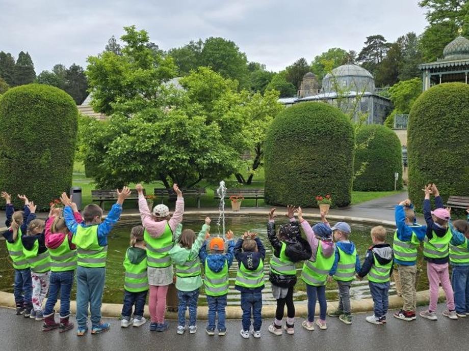 Spende eldorado Warnwesten Viele Kinder stehen mit ihren Warnwesten in der Wilhelma um einen runden Teich und strecken ihre Arme in die Höhe.