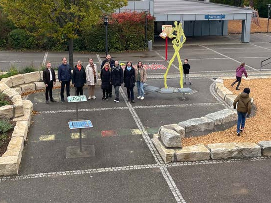Schulhofbegrünung Blick auf den neu gestalteten Schulhof mit mehreren Personen und Kindern an einem Spielgerät.