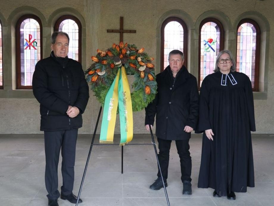 Totensonntag Friedhof Rutesheim Erster Beigeordneter Martin Killinger, Bauhofleiter Siegfried Kappus und Pfarrerin Angelika Rühle stehen in der alten Aussegnungshalle Rutesheim neben einem Blumenkranz mit Schleife.