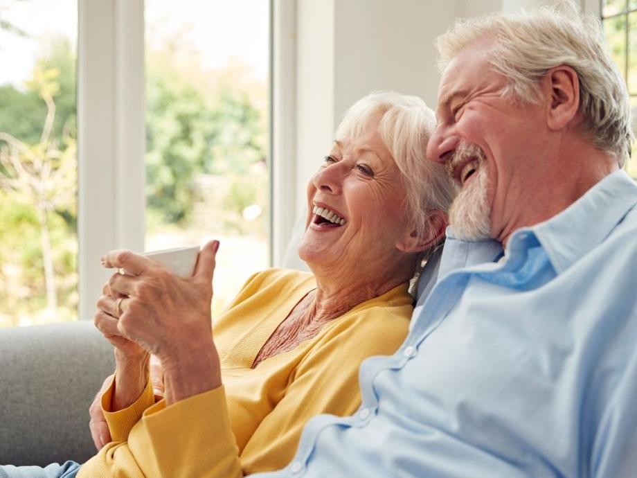 260305_monkeybusinessimages iStock-1440224128.jpg Ein älteres Ehepaar sitzt im Wohnzimmer auf der Coach, sie hält eine Kaffeetasse in der Hand.
