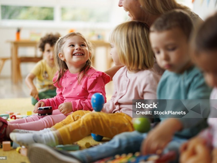 Kindergartenkinder Kindergartenkinder sitzen mit einer Erzieherin auf dem Boden und musizieren.