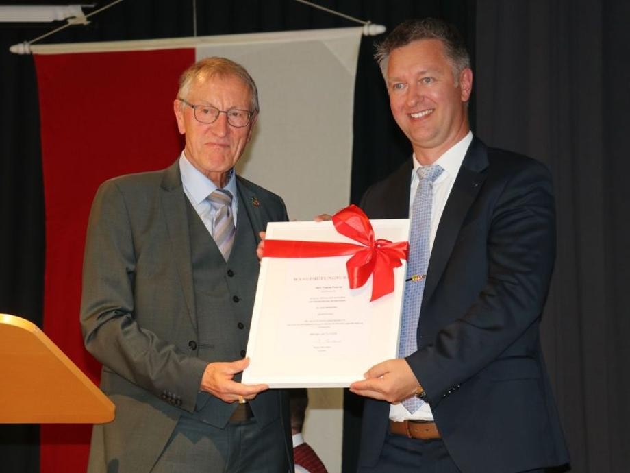 Amtseinsetzung BM Tobias Pokrop Landrat Roland Bernhard übergibt Herrn Bürgermeister Tobias Pokrop ein Geschenk verpackt in weißem Papier mit roter Schleife.