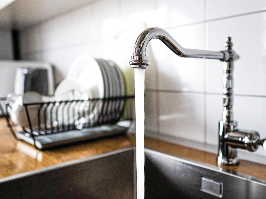 Wassersparen Spüle mit Geschirr in einem Metallständer und einem laufenden Wasserhahn.