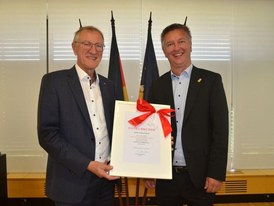 25. Dienstjubiläum Bürgermeister Pokrop Landrat Roland Bernhard übergibt Bürgermeister Tobias Pokrop die Jubiläumsurkunde in einem weißen Rahmen mit roter Schleife.