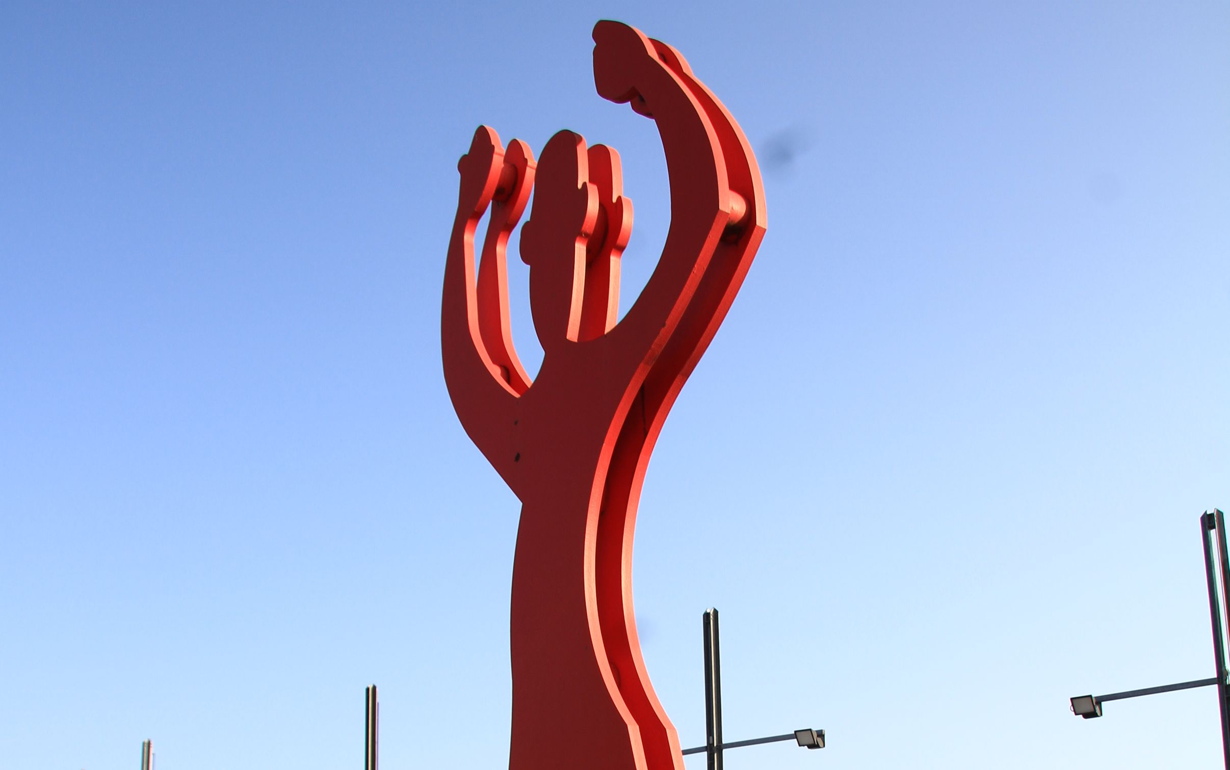 Rote Metall-Skulptur Mensch, der die Arme Richtung Himmel streckt.
