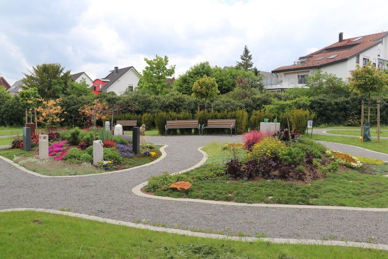 Blick auf das neu angelegte gärtnerbetreute Urnengrabfeld auf dem Friedhof Rutesheim mit vielen Blumen, Sträuchern und geschwungen angelegten Wegen.             