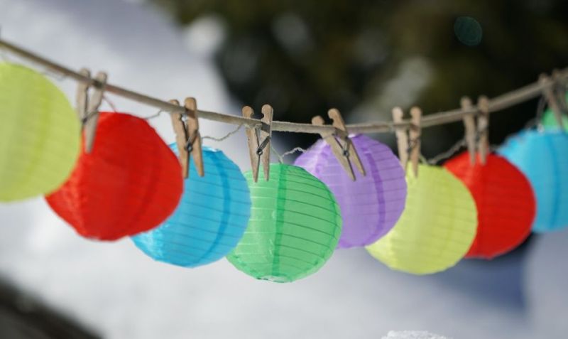 An einer Schnur hängen bunte Papierlampions, die mit Holzwäscheklammern befestigt sind.